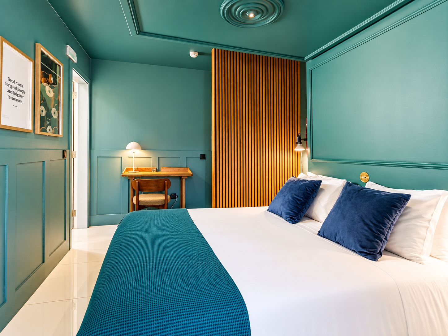 Habitación de hotel con cama, escritorio, silla y pared de listones de madera.