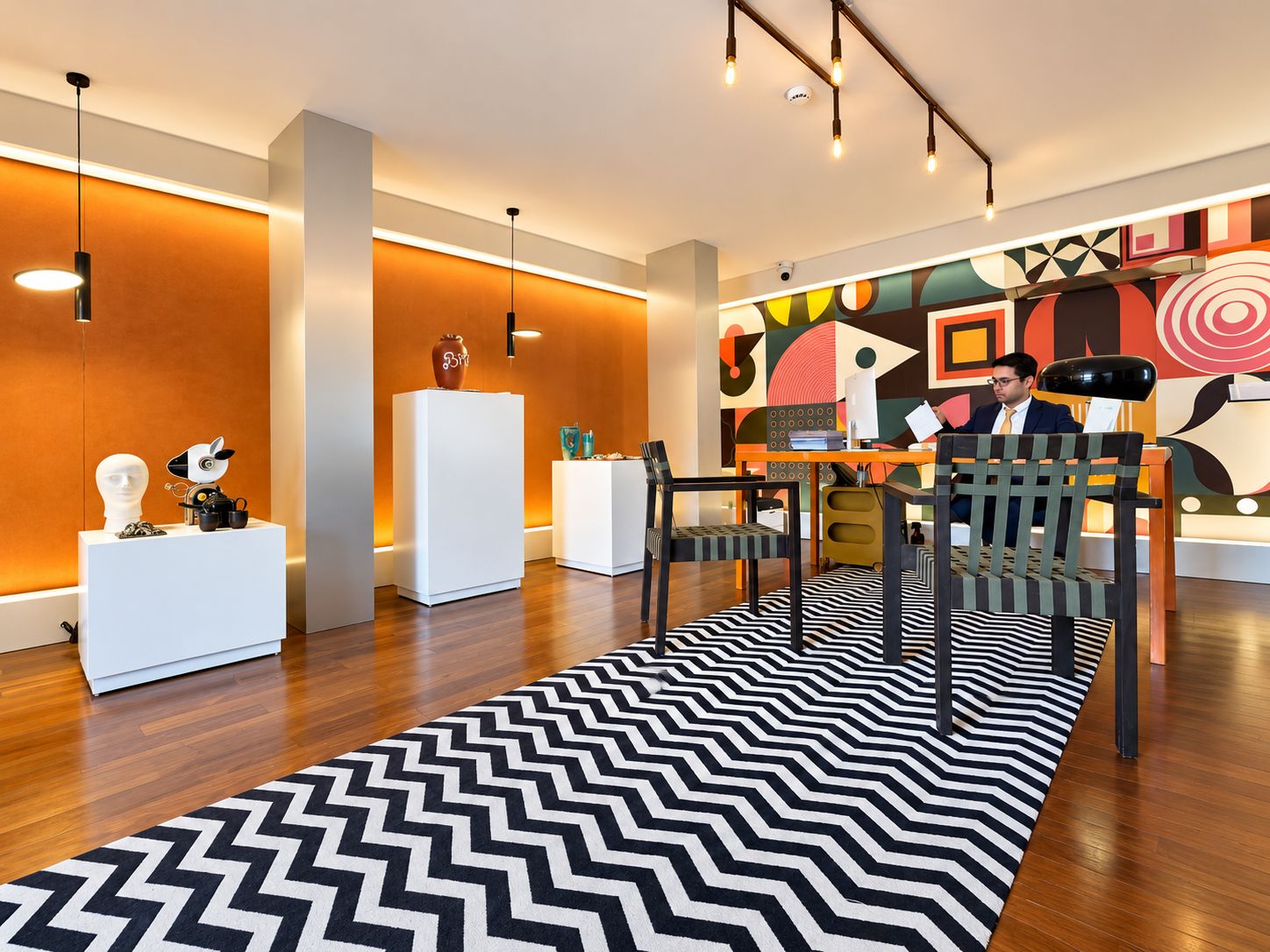 A modern hotel lobby with a geometric patterned rug, a reception desk, and a colorful abstract wall mural.