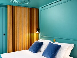 Una cama con almohadas blancas y azules, un cabecero de listones de madera y una habitación pintada en tonos verde azulado.