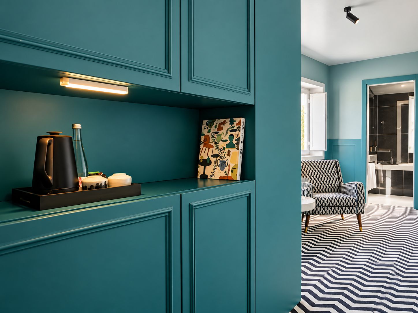 A teal-colored room with a modern design, featuring a coffee maker, a bottle, and a decorative item on a shelf.