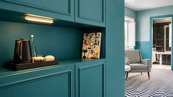 A teal-colored room with a modern design, featuring a coffee maker, a bottle, and a decorative item on a shelf.