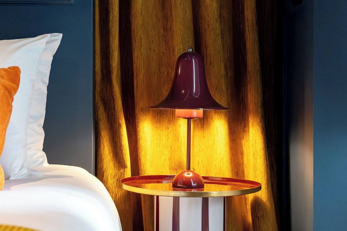 Ett hotellrum med en säng, ett randigt sidobord med en lampa och en gardin.