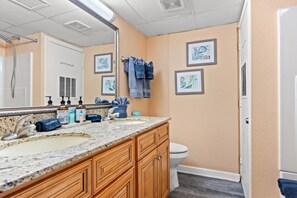 A bathroom with a marble sink, wooden cabinets, a toilet, and framed artwork on the wall. - Oceanfront Condo Stay with Heated Pool and Hot Tub (North Myrtle Beach)