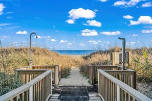 A wooden pathway leading to a beach with a clear sky and clouds.