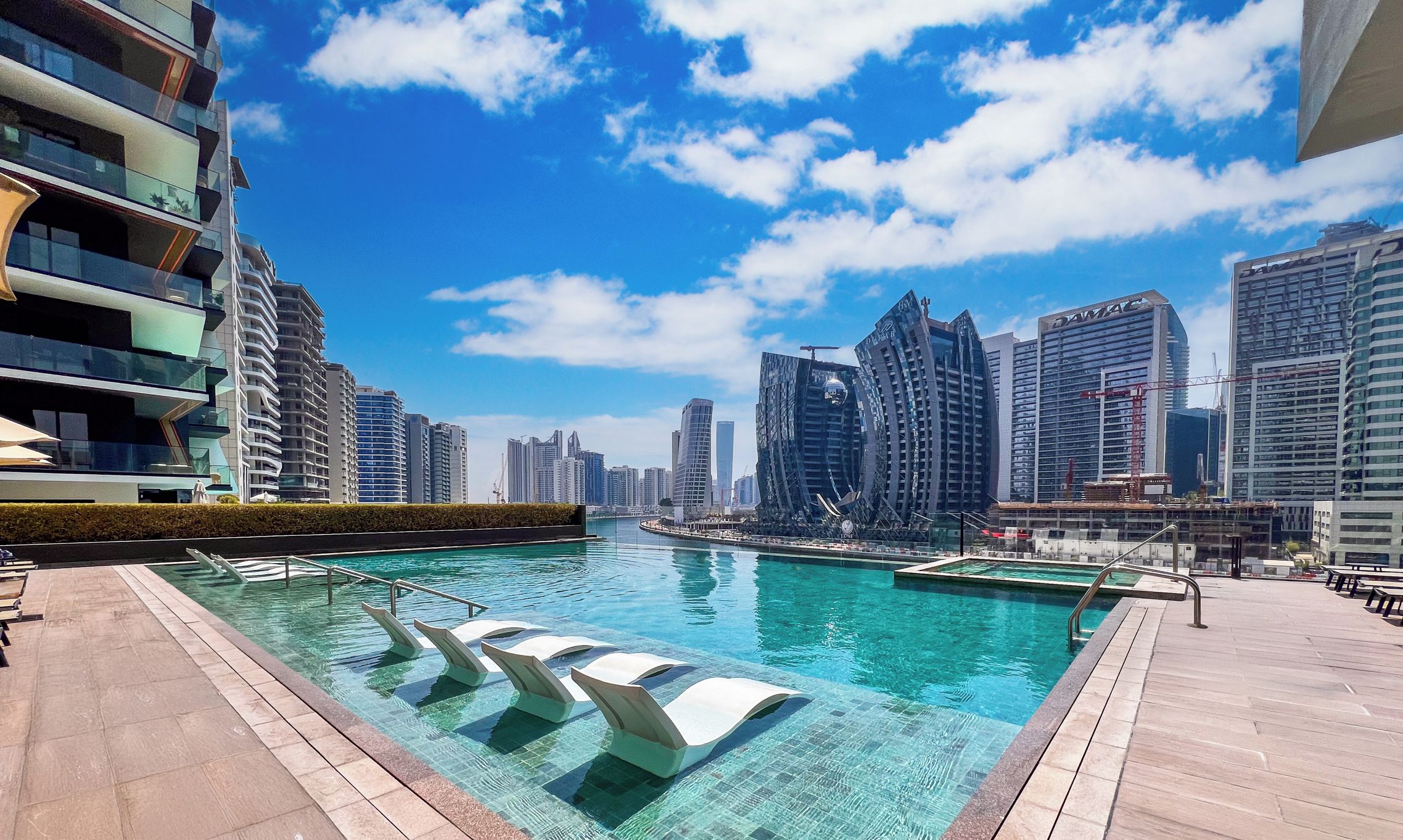 A pool area with clear water, surrounded by modern buildings and a city skyline.