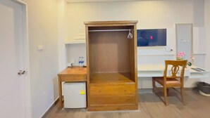 Habitació compacta amb escriptori de fusta, nevera petita, televisió penjada a la paret i una cadira amb coixí.