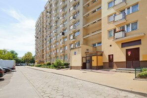 Un edificio residencial de varios pisos con balcones, una entrada con reja y una calle pavimentada al frente.