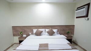 Une chambre d’hôtel avec un grand lit, deux tables de chevet, un climatiseur fixé au mur et une tête de lit en bois.