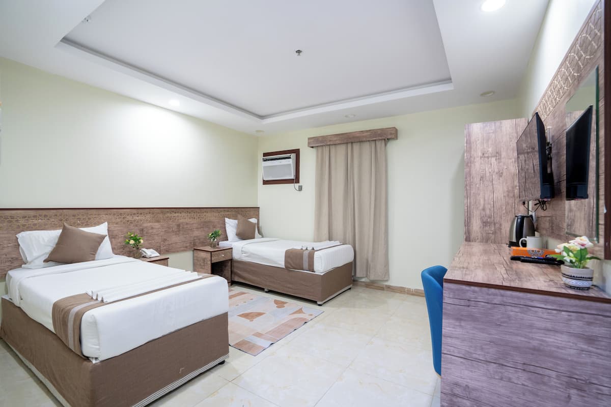 A hotel room with two beds, a desk, a mirror, and a television.