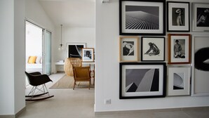 A modern living room with a large window, a black rocking chair, a wicker chair, and a dining area with a table and chairs. - Villa Arte – Modern villa in Biot with private pool (Biot)