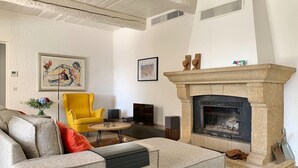 Un salón con chimenea de piedra, un sillón amarillo, un sofá gris y obras de arte en las paredes.