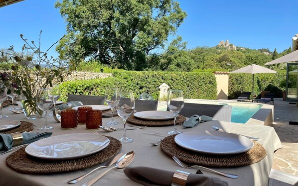 An outdoor dining setup with tables, chairs, and a pool in the background.