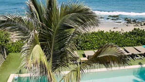 Piscina com vista para o oceano, cercada por palmeiras e espreguiçadeiras.
