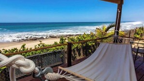 Une vue sur la plage depuis une terrasse couverte, avec un hamac et des cordes.