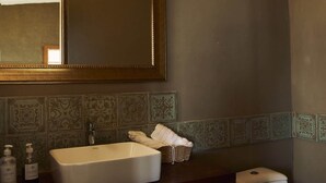 Une salle de bain avec un lavabo rectangulaire, un miroir au-dessus, et des toilettes avec deux rouleaux de papier toilette.