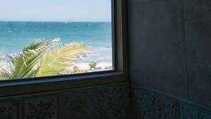 Une salle de bain dotée d’une grande fenêtre donnant sur l’océan, d’un mur carrelé et d’un luminaire au plafond.