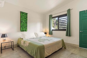 Una camera da letto con un letto, un comodino, una lampada, una finestra con tende e una porta verde.