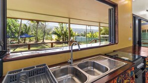 Cocina con un ventanal amplio, pileta de acero inoxidable y vistas a un paisaje tropical.