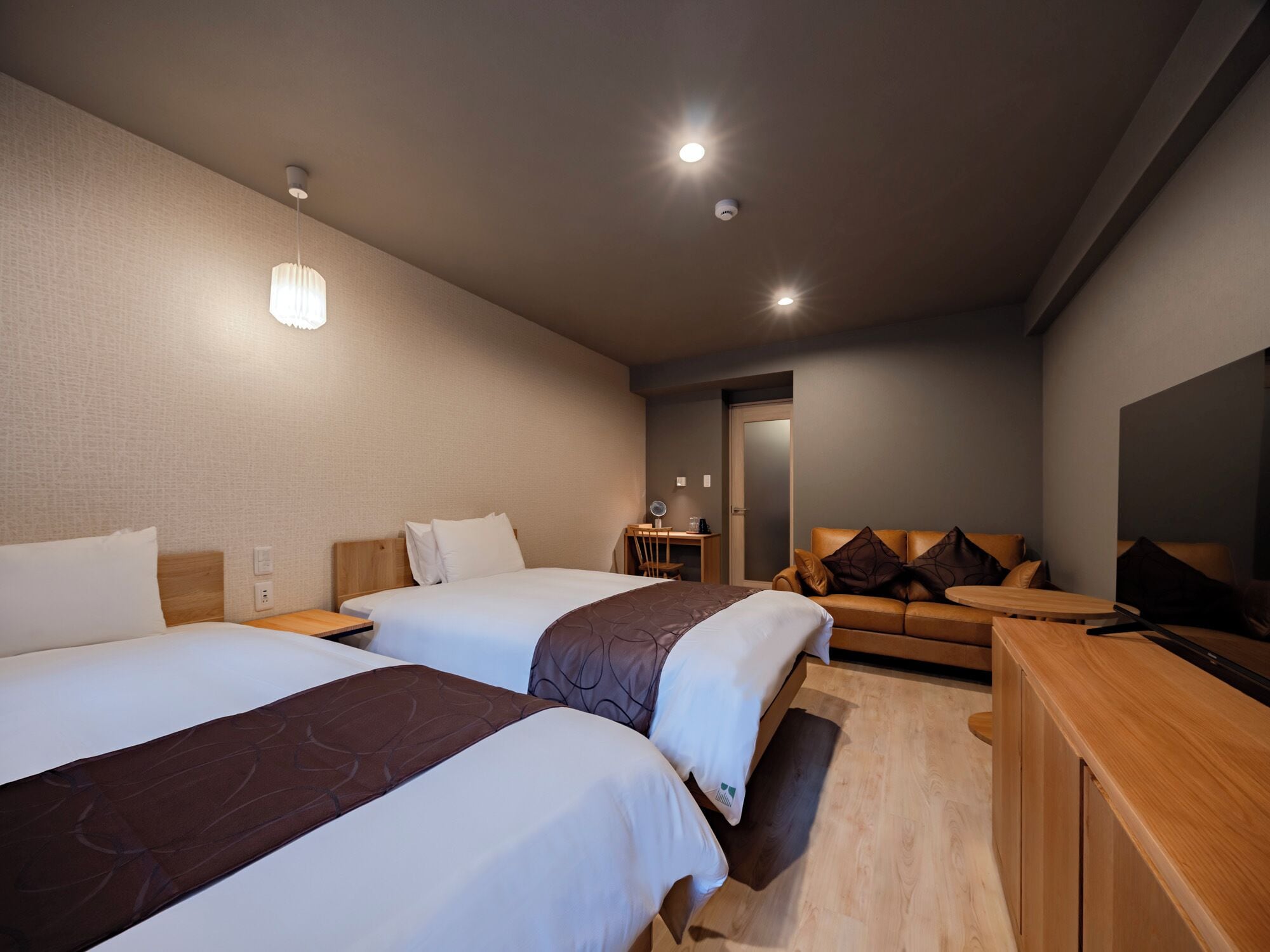 Ein Hotelzimmer mit zwei Betten, einem Sofa, einem Schreibtisch und einem Fernseher.