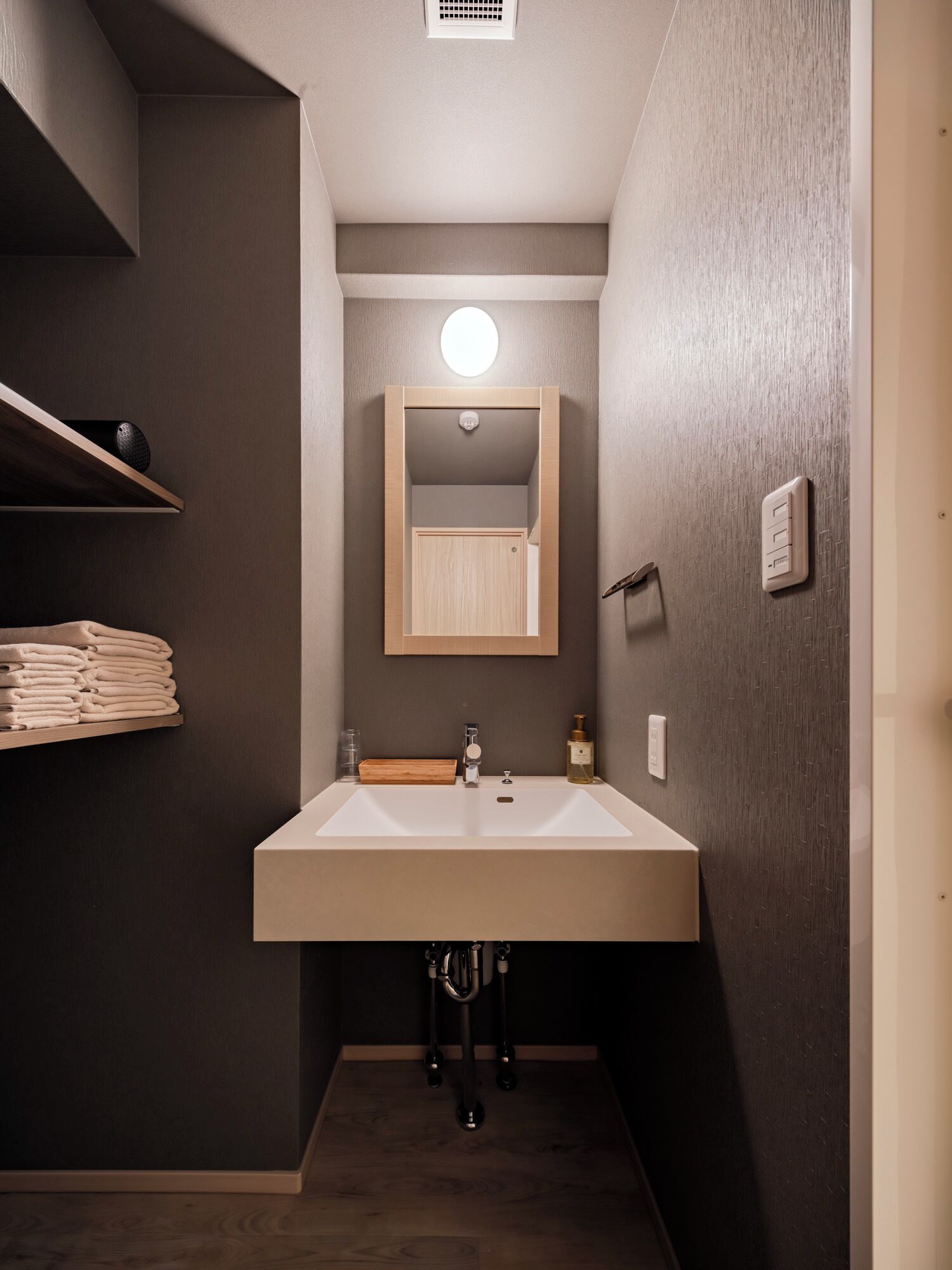A modern bathroom with a large sink, a mirror, and a shelf with folded towels.