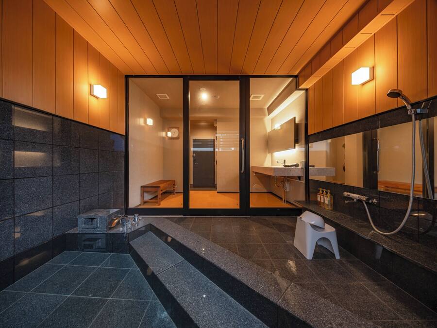 Un baño moderno con techo de madera, una puerta de vidrio que da a la zona de ducha, un banco y un lavamanos con espejo.