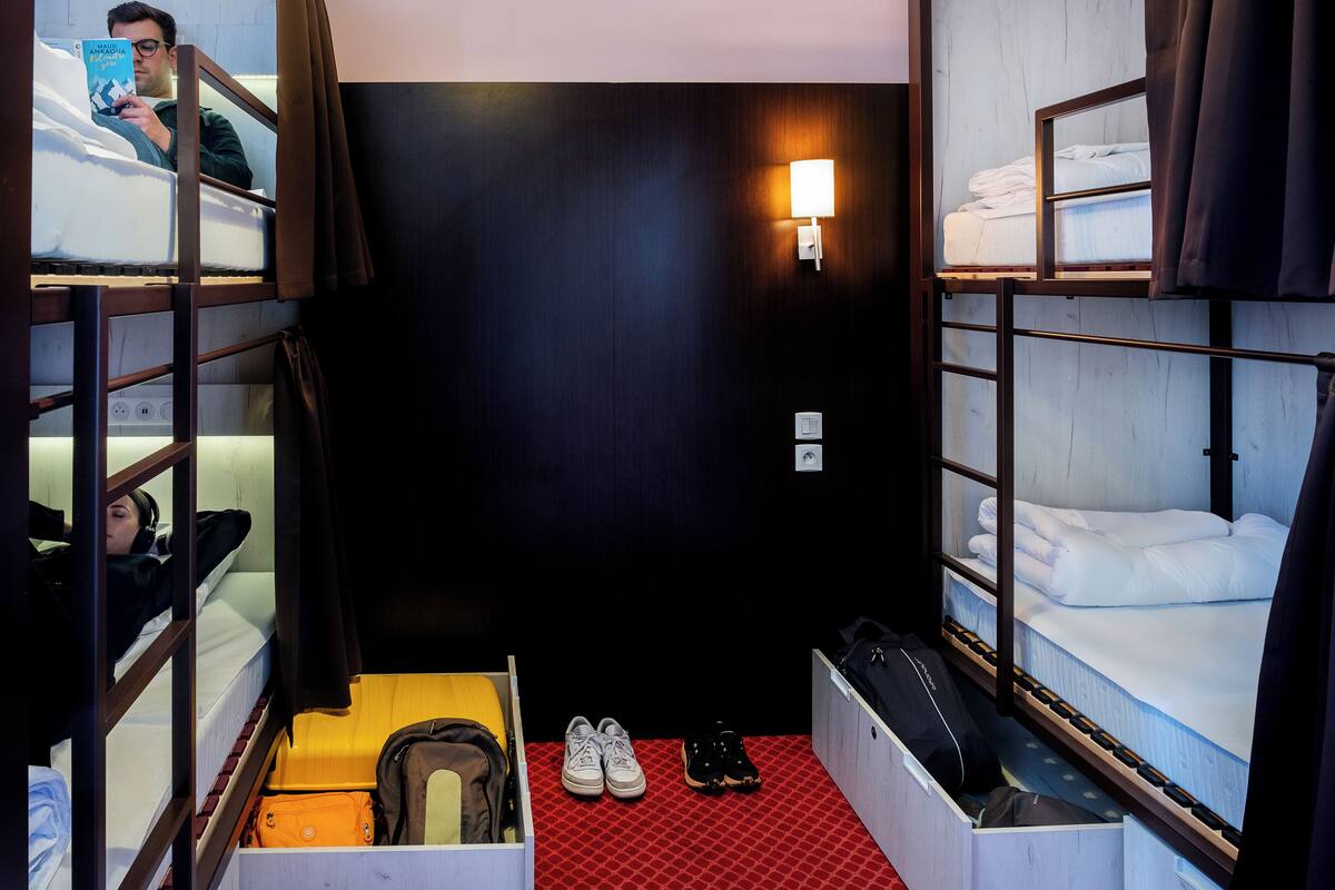 A compact hotel room with bunk beds, a red carpet, and a wall-mounted light fixture.