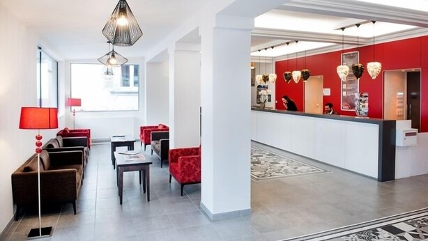 A hotel lobby with a reception desk, red upholstered chairs, a coffee table, and a floor lamp. - Rosalita Hostel (Lourdes)