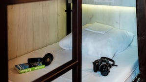 A neatly made bed with a pillow and a book titled "Pyrénées" on a shelf beside it. - Rosalita Hostel (Lourdes)