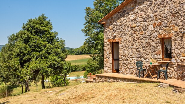 Un bâtiment en pierre doté d’une terrasse, de sièges extérieurs et offrant une vue sur un paysage verdoyant.
