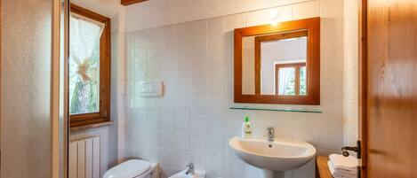 A bathroom with a toilet, bidet, and sink, wooden ceiling, and a window with a view.