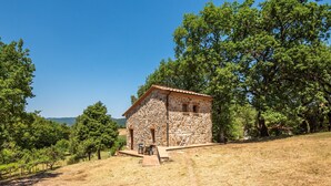 Un bâtiment en pierre, doté d’un toit en tuiles, entouré d’arbres et bordé d’un paysage verdoyant.