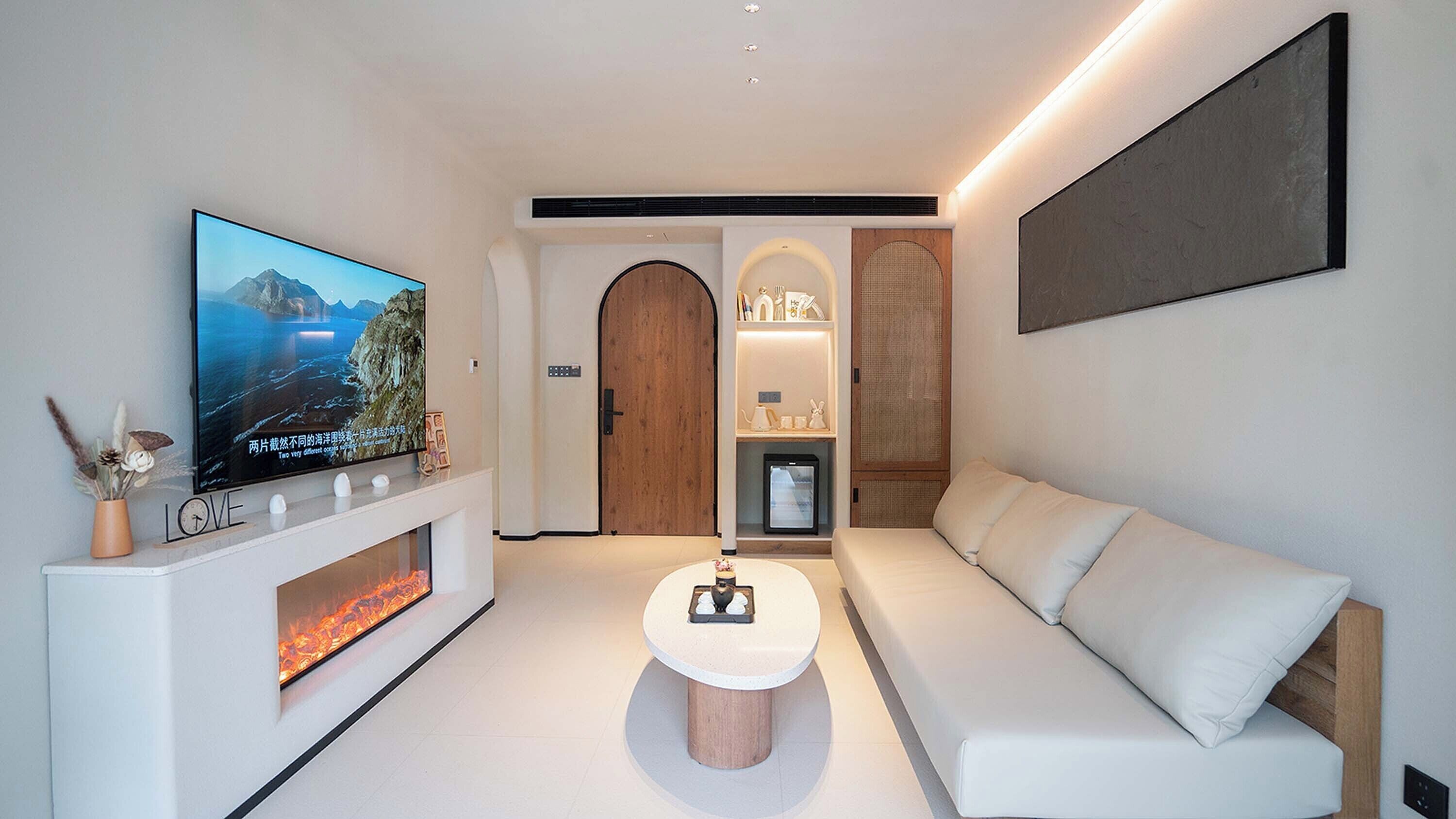 A modern living room with a flat-screen TV, a fireplace, a white sofa, and a coffee table.