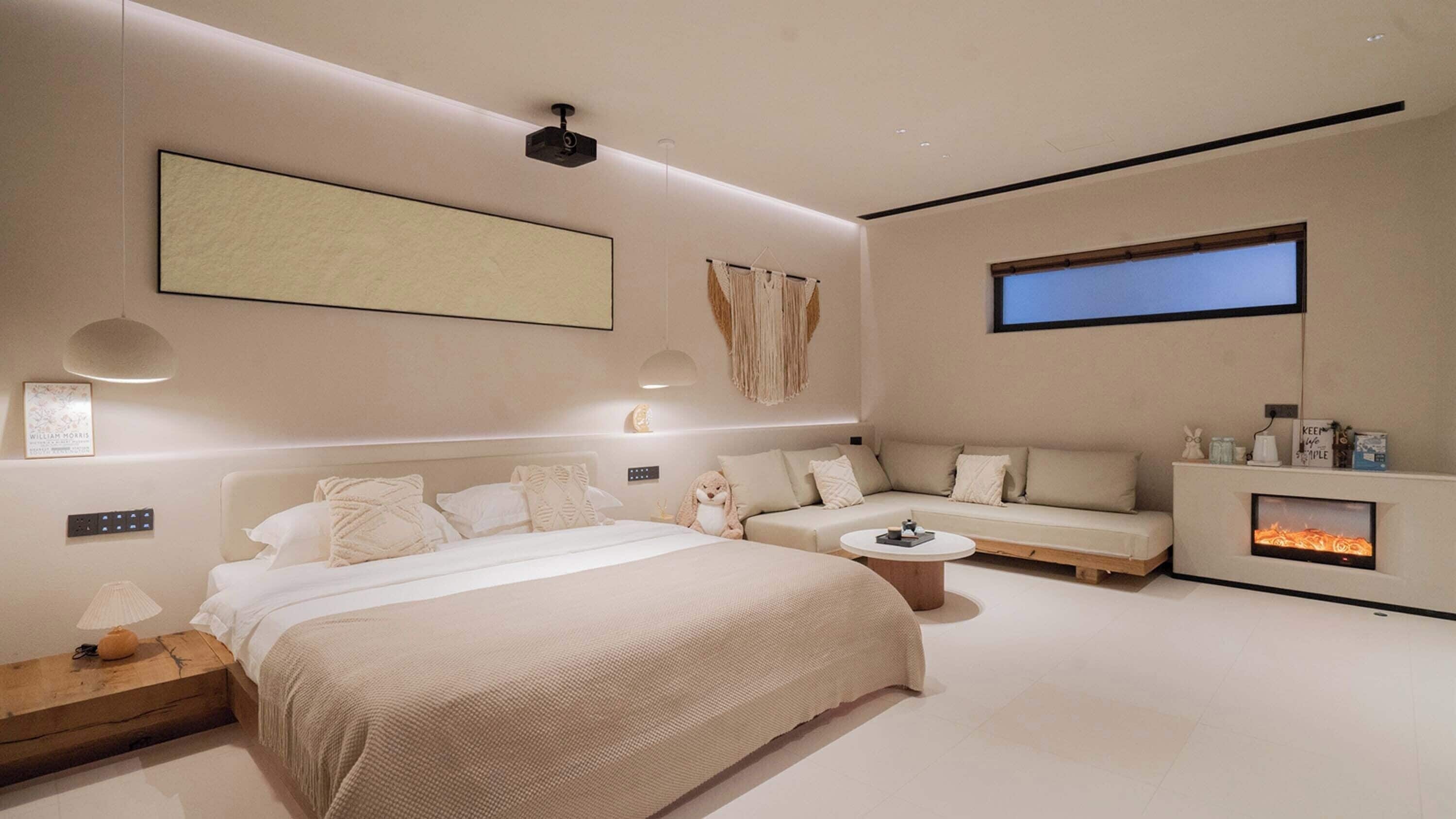 Quarto moderno com uma cama grande, um sofá, uma mesinha, lareira e TV fixada na parede.