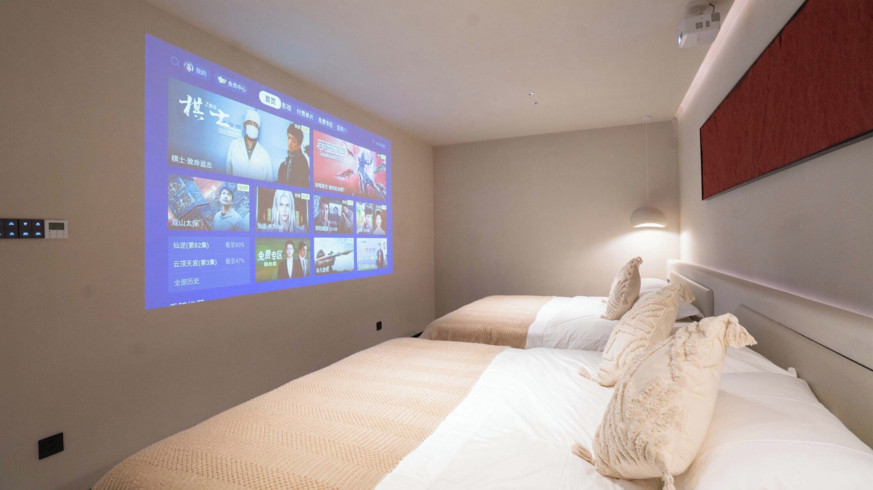Una habitación de hotel con una cama, un proyector de pared que muestra una película y una mesita de noche.