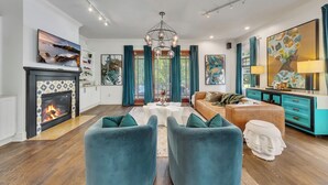 A modern living room with a fireplace, teal chairs, a sofa, and artwork on the walls. - Modern eclectic 4BR, 3BA home in the heart of Inman Park. (Atlanta)