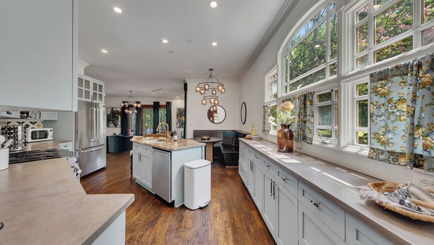 A spacious kitchen with a central island, white cabinetry, and a large window with floral curtains. - Modern eclectic 4BR, 3BA home in the heart of Inman Park. (Atlanta)