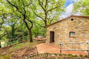 Ein Steinhaus mit Tür und Fenster, umgeben von Bäumen und einem eingezäunten Bereich.