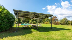A covered picnic area with benches and a pool in the background.