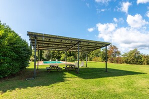 Un área de picnic techada con bancos y una piscina al fondo.
