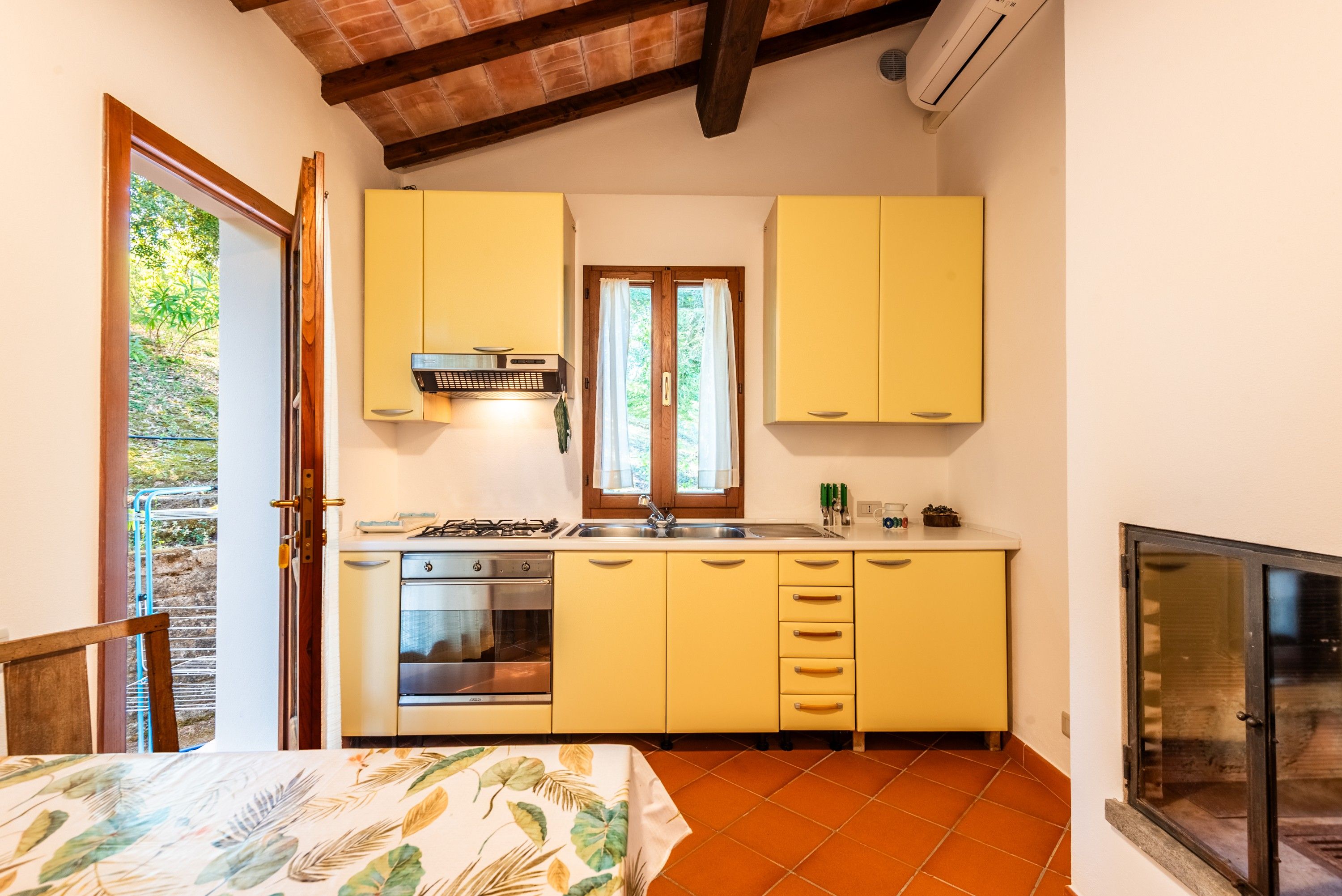 A compact kitchen with yellow cabinets, a built-in oven, and a window with curtains.