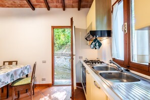 Une cuisine de taille réduite, équipée d’une cuisinière à gaz, de deux éviers et d’une fenêtre donnant sur un jardin.