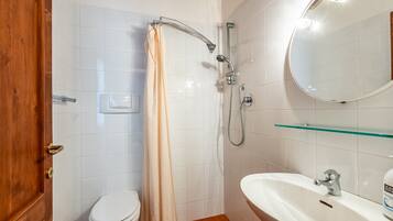 A bathroom with a toilet, a shower with a glass shelf, and a sink with a mirror.