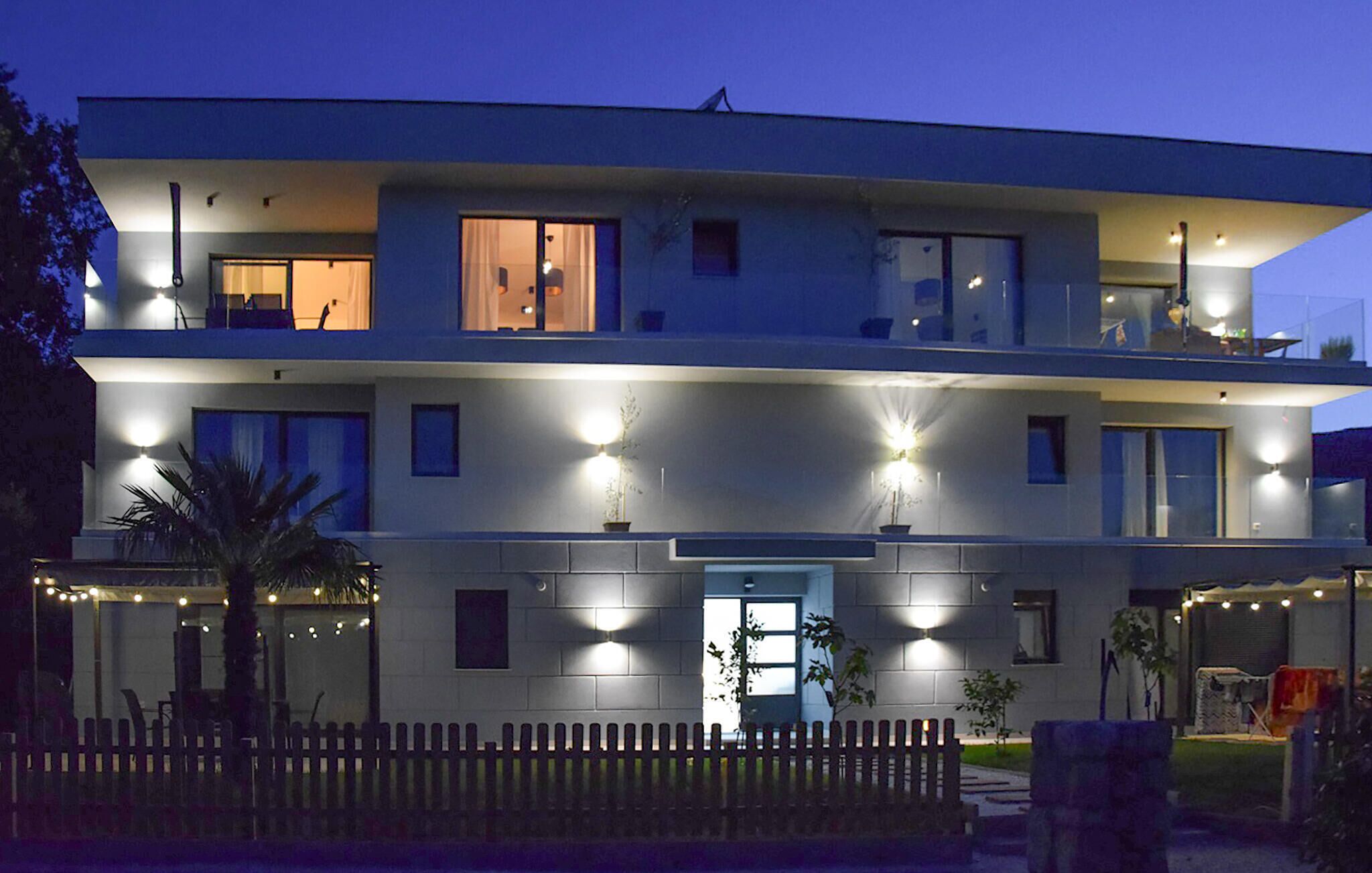 A modern two-story building with multiple illuminated windows and balconies.