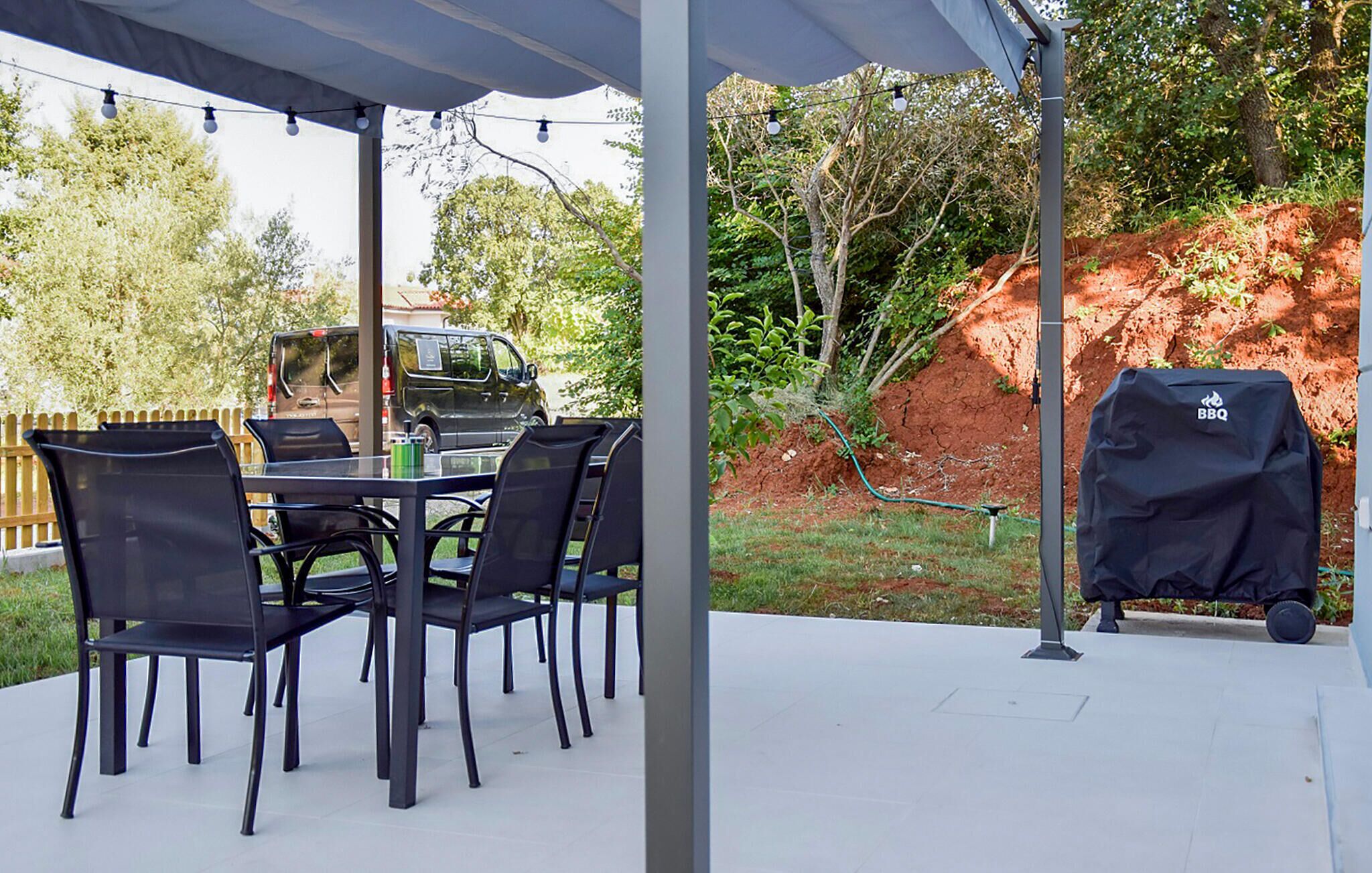 An outdoor patio with a table and chairs, a barbecue grill, and a covered area with string lights.