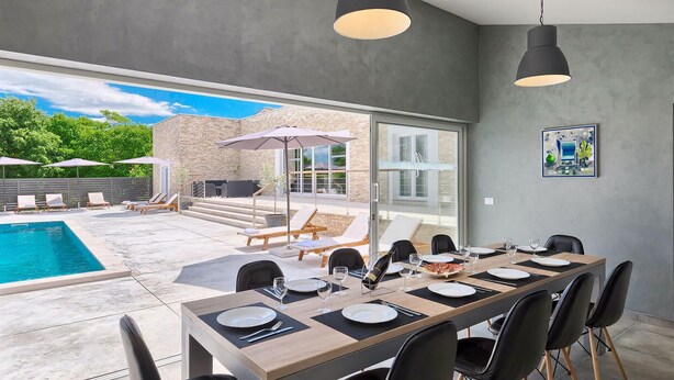 A modern dining area with a pool view, outdoor seating, and a stone building in the background. - Beautiful home in Rovinjsko selo (Rovinjsko selo)