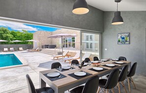 Un espace repas moderne avec vue sur la piscine, des sièges en plein air et un bâtiment en pierre en arrière-plan.