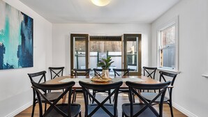 Un coin repas avec une table en bois et des chaises noires, une plante en pot et un grand tableau abstrait accroché au mur.