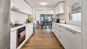 Une cuisine moderne avec des meubles blancs, un plancher en bois et un coin repas comprenant une table et des chaises.