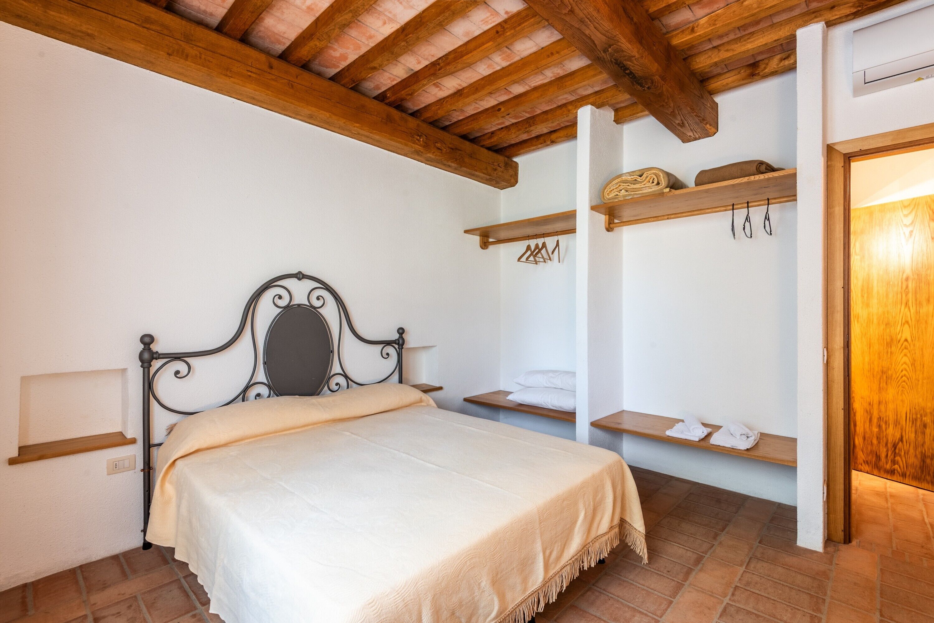 A bedroom with a bed, wooden beams, a white wall, and a wooden door.