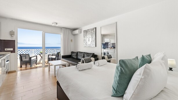 A modern hotel room with a large bed, a balcony with a view, a dining area, and a kitchenette. - Apartamento Mar Azul (Puerto del Carmen)